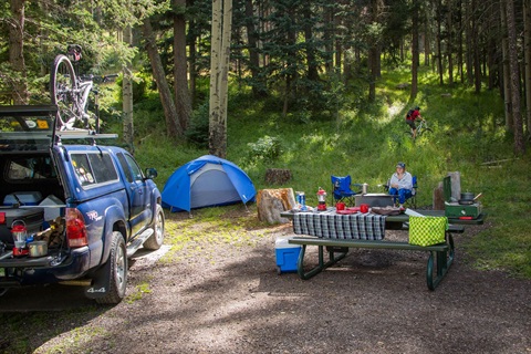 Camping at Camp May with a tent, truck with supplies, mountain biker, and person sitting at the campfire