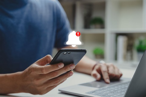 Service Alert Stock Image showing a person holding a cellphone with an alert bell above it and touching a laptop