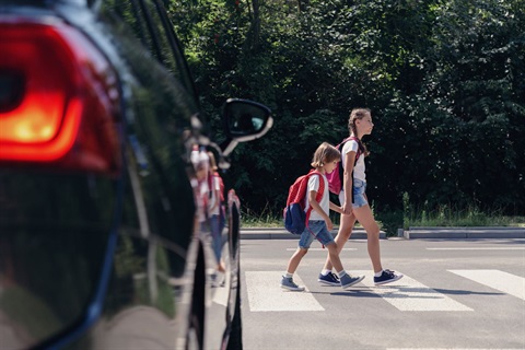 Pedestrian Crossing where two young girls are walking in the sidewalk in front of a car