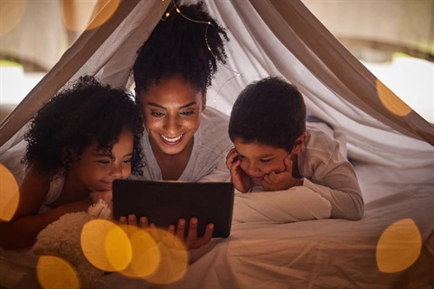 Mother and two children reading a book in a blanket fort