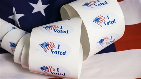 Roll of I Voted stickers with an American flag behind it