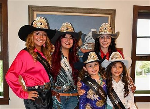 Photograph of the newly crowned 2024 Royalty Court (three young women and two young girls) smiling and wearing matching cowboy hats and colorful western shirts and dresses. They are indoors and standing in front of a painting of indigenous pottery.
