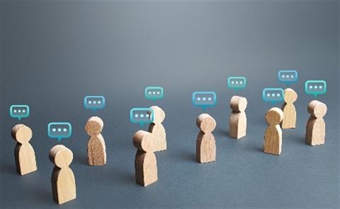 Wooden figure representations of people with word bubbles with three dots in them above each head on a plain blue background